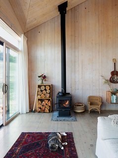 The restrained 820-square-foot interior is defined by the angular ceiling. Garlick left the prefabricated structural panels unfinished to save on material costs. A True North wood stove from Pacific Energy heats the house. Max, the family’s cat, naps on a vintage rug purchased on eBay.<br>