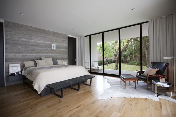 In the master bedroom, the textural appeal of the reclaimed wood wall, bedding, and rug contrasts with the black leather of the African-inspired ‘Bwana’ Chair by Finn Juhl, which sits beside a ‘TAB’ reading lamp by Barber Osgerby. “We believe a quality project is defined by the sum of all its parts versus any individual feature or design move,” Field says. Photo 6 of Preston Hollow modern home