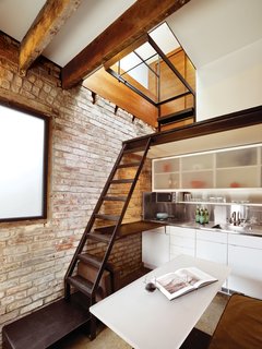 A Compact Three-Story Brick Loft in San Francisco - Photo 1 of 3 - Architect Christi Azevedo deployed Ikea cabinetry in the kitchen (left), which spans almost the entirety of the renovated building. In lieu of adding standard-issue fronts to the upper cabinets, she created sliding doors of sanded acrylic panels. A PaperStone work top extends from the stainless steel counter for additional prep space. When not in use, the movable dining table—also designed and fabricated by Azevedo—fits snugly beneath it.