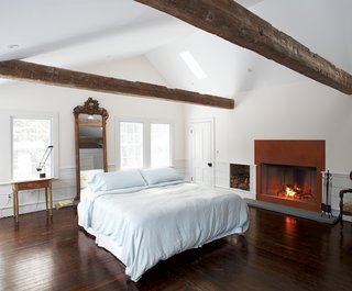 A gas fireplace fronted in weathered steel warms up the lofty master bedroom, whose spare decor is framed with beams discovered in a Pennsylvania barn. The Tizio desk lamp is by Artemide.