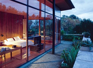 Dappled sunlight and reclaimed-wood floors and walls give the master bedroom a warm, peaceful feel. Giant sliding doors open onto a wraparound deck peppered with potted plants <br><br>from the couple’s vacations in Brazil, Uruguay, the Netherlands, and Italy.