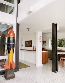 A Home's Past Mistakes Are Finally Corrected - Photo 10 of 14 - The entrance opens to the living area, in which an I-beam stands where the kitchen enclosure was. "It was really tight, so we wanted to push back the wall that was in front of the door," Julien says. The couple traded the old carpet for terrazzo flooring. Julien found the test bomb at an antiques mall.
