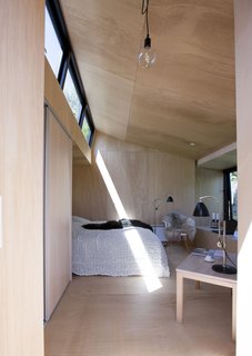 The interior is small, but comfortable. It fits a double bed, coffee table, and chair. The bed is recessed into the wall so as not to waste any space. Natural light floods the interior from a clerestory.