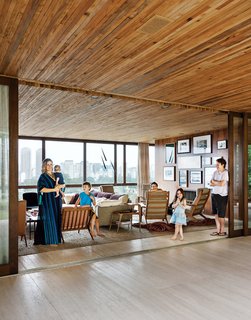 With São Paulo on one side and a terrace and garden on the other, the Strozenbergs’ living room feels vast. The sofa is a Harry Large by Antonio Citterio for B&B Italia and the coffee table behind Ticiana Strozenberg (with baby) is a vintage design by Geraldo de Barros. The custom wood paneling throughout the house is by Fiamoncine, as are the window treatments.