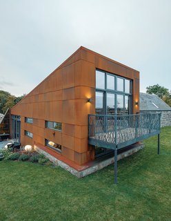 This Farmhouse is a Cor-Ten Steel-Clad Dream - Photo 8 of 11 - McAvoy rebuilt the farmhouse’s original stone walls piece by piece. The couple found the sofa and ottoman at a local shop, Annie Mo’s. For the new structure, Grace & Webb fabricated a laser-cut steel balcony.