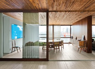 A wooden partition separates the dining room from the living room. The jacaranda table is a vintage find designed by Jorge Zalszupin for L’Atelier. The dining chairs are by the Brazilian designer Sergio Rodrigues and architect Isay Weinfeld designed the sideboard. The fluorescent lamp sculpture on the wall is Luz Natural by Eduardo Coimbra.
