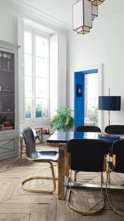 The dining room features 1970s leather-and-brass dining chairs and a table concocted from a brass-and-silver base and a custom lacquered top. The cheerful blue paint enlivening the doorway is from Emery & Cie.