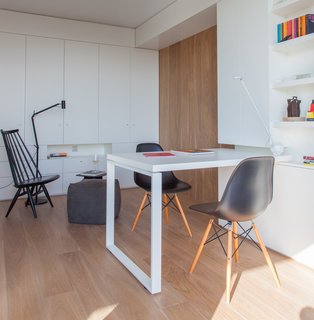 A sliding oak door leads from the living room to the studio library, outfitted with custom, white-lacquered built-in units and furnishings. The floor lamp is by Marset, and the MDM lounge chair and poufs, all from Materia, form a cozy reading nook.