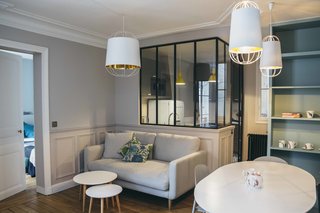 10 Dreamy Parisian Homes - Photo 7 of 10 - The addition of custom steel-and-glass windows significantly opened up the apartment, adding visibility and light between spaces in this family-centric environment. Muted blues and grays in pastel tones keep the space feeling soft, cool, and relaxed, while the Conran Pembury sofa, La Redoute tables, and Petite Friture pendants add a distinctly contemporary air.