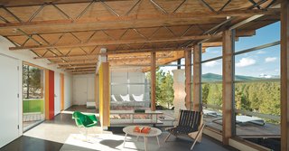 The architects wrapped the glazing around the corner of the living room to bring the landscape inside. The open-web trusses run continuously from indoors to out. A fleet of Modernica furnishings complement a Prototype Boomerang chair by Richard Neutra, a custom Moufelt industrial felt rug, and Circa50 butterfly chairs.