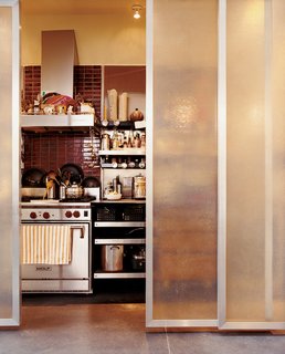 The kitchen and Baker's home office, which has artwork and inspiration pinned above the desk, are aligned behind sliding fiberglass-and-bamboo shoji screens. Devoid of cabinetry, the kitchen is fitted out with industrial cantilevered shelving from E-Z Shelving Systems in Kansas City. The red tiles behind the stove are from Heath Ceramics.