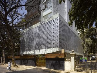 A view from the street reveals the front and side elevations of the building, with somewhat of an architectural refrain of perforations running up the side of the apartments. The balconies, made from a recycled Indian railway hardwood, employ closely linked slats whose gaps widen as they go up, to allow breeze and light in. To their right are the apartments' bedrooms.