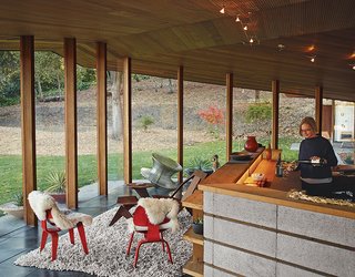 Lambert pours wine in the kitchen, which is defined by a low concrete-block wall and serves as the home’s central core. The seating-area chairs are from Herman Miller.