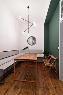 Our Dorm Definitely Did Not Look Like This - Photo 4 of 7 - Two green accent walls—one seen here in the dining room—are the only departures from the strategically white backdrop. Wierciński and team designed the dining table and its orange steel frame, along with the seating benches and wall-mounted seat backs. A Sticks pendant light from Nowodvorski illuminates the space.