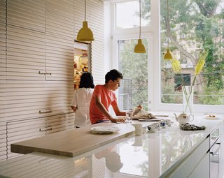 The white-oak palette continues in the kitchen, where full-height cabinets are made with handcrafted, slatted detailing that wraps up the ceiling, and back down around to an opposite wall of drawers. The island countertop is made of Glassos, a durable, crystal-glass material. It is partially topped with a white-oak slab, with a slight overhang that makes for an apt workspace. The pendants are by Caravaggio, and the dishwasher is by Bosch.