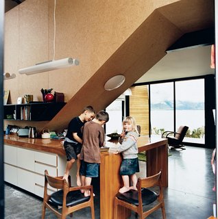 The kids, Archie, Linus, and Olive, stand in the kitchen, beneath the strand board–clad stairwell that leads to the bedrooms. Kerr and Ritchie initially envisaged rich materials for the interior, but changed their minds in favor of what they call a "cartoony" approach with cheaper, hard-wearing elements. "We didn’t want the space to feel too grown-up," Kerr says.