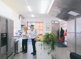 Lawrence and Alice confer in the ground-floor kitchen. Traces of color are visible everywhere, including the orange-and-yellow curtains and pink coat hooks.