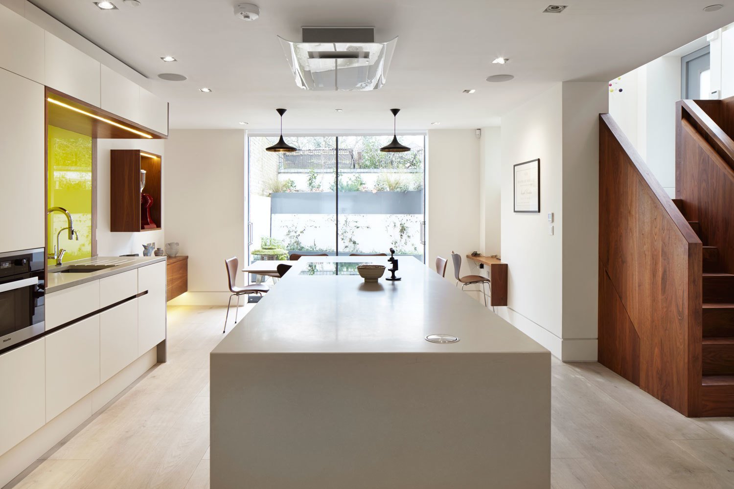 The formerly dark basement kitchen now feels much lighter, thanks to the addition of white oak floor boards, bright plaster walls, and floor-to-ceiling windows that let in garden views.