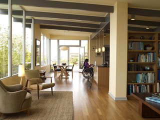 The main living area, which includes a more formal sitting area near the entrance, the dining area, Braitmayer’s workspace and the kitchen, in which the couple’s daughter works at the island. In the foreground is a pair of mid-century chairs; at left is a Heywood-Wakefield that Braitmayer found at an antiques shop. Seattle-based designer Lucy Johnson completed the interiors. The windows are from Lindal, and the exterior doors are from Marvin.
