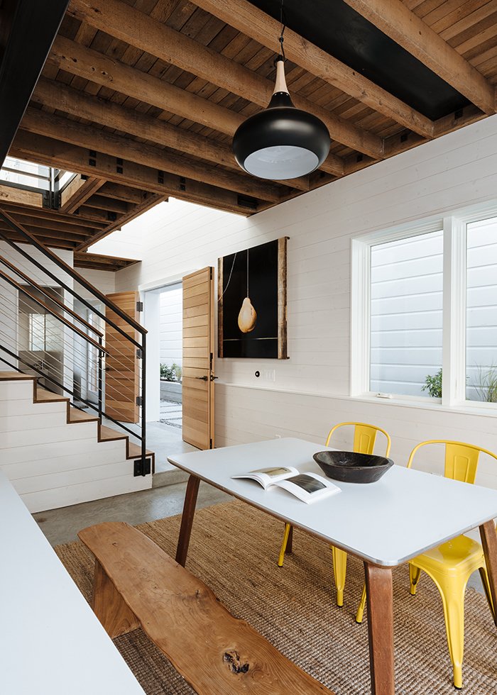 Throughout the house, Curtiss mixed natural materials with industrial ones. Downstairs, fir and cedar wood on the doors and open-joisted ceiling balance the colder, industrial feel of the concrete floor and steel staircase railing. In the dining room, a pendant lamp from RLM Lighting hangs above a table that combines Cherner table legs with a new white laminate top. The yellow chairs are by Tolix.