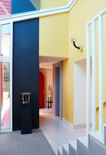 Color Me Mad! - Photo 17 of 31 - Vignettes of contrasting colors, materials, and shapes frame every corner. A one-of-a-kind chair by Peter Shire sits in the hallway; near the sculptural staircase is a sconce for Yamagiwa and a sterling silver centerpiece for Memphis, both by Sottsass.