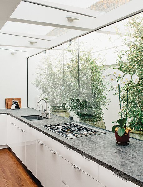 This new kitchen borrowed space and light from the original courtyard. The spirit of the courtyard remains with the buffer between the kitchen and the exterior wall. The cabinets are from Ikea, the countertops are quartzite, and the grill top is from Bertazzoni.