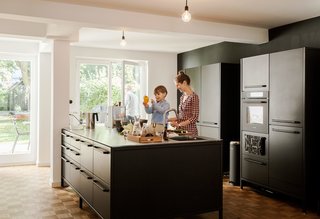 We Can't Get Enough of This German Apartment's Sleek Matte-Black Kitchen - Photo 2 of 11 - The island serves as a generous workspace for Dorothee to prepare dishes with her son Morten. The couple’s updates to the 1967 apartment included introducing large windows to the garden and covering the floors with an oak parquet to match the original flooring in a couple of rooms.