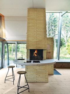 Inside, life revolves around the brick chimney, which the architect surrounded with a concrete counter that wraps from the kitchen to the living area. The stools are vintage.