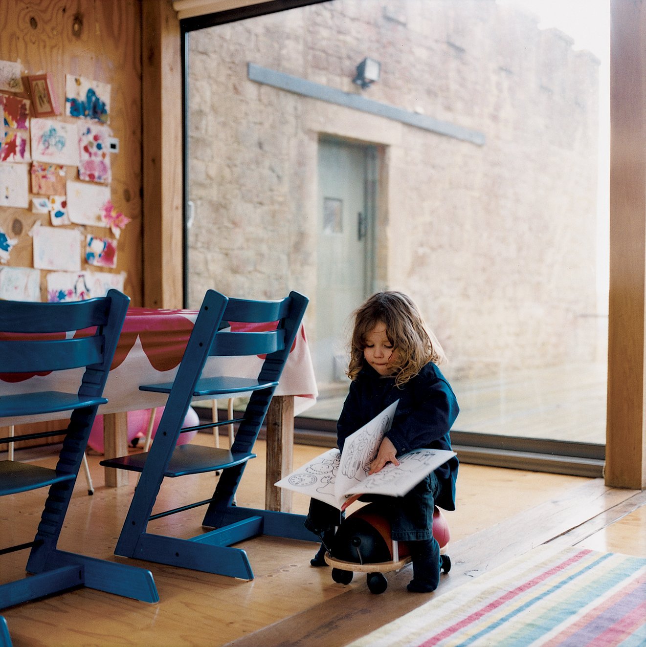 The main living room is an open-plan space with an integrated kitchen and dining area. The table, made by Taylor and shrouded in Marimekko, is outfitted with blue Tripp Trapp adjustable children's chairs by Stokke; the striped rug is from Ikea.