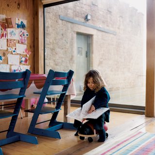 The main living room is an open-plan space with an integrated kitchen and dining area. The table, made by Taylor and shrouded in Marimekko, is outfitted with blue Tripp Trapp adjustable children's chairs by Stokke; the striped rug is from Ikea.