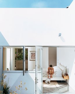 Dawn Farmer sits on the bed in the master bedroom. The white leather bed was designed by Pierre Kozely and manufactured by Della Robbia. The view carries through the master bathroom to the yard on the other side of the house.
