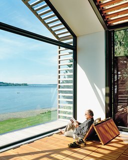 Renovated Garage is the Ultimate Modern Party Space - Photo 5 of 9 - The Trues host parties in the glass-walled structure, located steps from their vacation home, or they escape to it to catch some rays and read a book. Bill reclines on cushions hidden under the reclaimed-fir floorboards that are propped up with Sugatsune hinges.