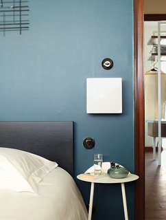 Modern Home Furnished With Flea Market Finds - Photo 6 of 17 - Farrow & Ball’s Hague Blue covers a wall in another bedroom. The light switches here, and throughout the apartment, are Hager’s 1930 series. Deau stationed a 1970s-era sconce next to the bed.