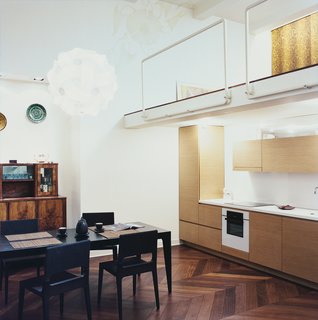 Palace Intrigue - Photo 10 of 13 - The kitchen fits neatly on one wall. The architect reads at a black Ligne Roset dining set, beneath a Col pendant lamp by Francisco Luján. The tublar steel mezzanine rails were designed by Mikulionis, who enjoyed being exempt from the safety concerns that a client would force on him.