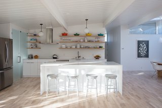 Sunny Renovation of an Eichler Great Room - Photo 2 of 5 - The updated kitchen features a bright white palette. The countertop is Caesarstone's Blizzard surface and the stools are Crate and Barrel. The range hood is Futuro, the refrigerator is LG, and the dishwasher is Bosch.