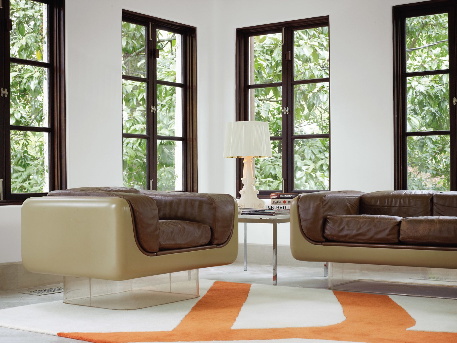 To highlight the existing architecture of the home, Hill retained the dark polish of the casement windows, which she finds enhances period details instead of undermining them. In the rear sunroom, the vintage Case Study furniture pieces with Plexiglas bases are from Metro Retro in Houston.<br><br>A Bourgie lamp by Kartell is atop an old marble end table by Knoll, and the Gan kilim rug pictures a branch motif echoed in the kitchen and breakfast room.