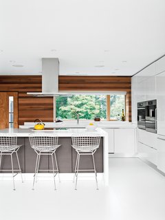 The Midcentury Spirit is Alive and Well in This Hudson Valley Escape - Photo 4 of 11 - Bertoia bar stools by Knoll are tucked under the island in the Scavolini Scenery kitchen. Fernando Franco of floor specialists Garage and Beyond replaced the original wood flooring with white resin, a robust surface used in high-traffic environments.