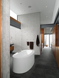 In the master bathroom, the couple traded an outdated tile tub for the BOV 02 from Wetstyle and added fixtures, towel bars, and hooks from Vola. The hallway, which retains its original black granite floor, leads past paneled walls to a deck.