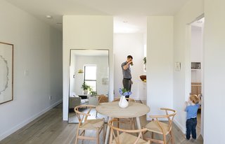 A large metal floating mirror from Restoration Hardware seemingly doubles the 675 square feet of the Schmidt-Friedlander apartment in Windsor Terrace, Brooklyn. The family of three dines at an oak table from Canvas Home, with Wishbone chairs by Hans Wegner. Decorators White paint by Benjamin Moore and oiled Hakwood European oak flooring are used throughout.