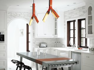 Hill had the overhead lighting in the kitchen customized by Rich Brilliant Willing in a pert orange that accents the primarily black-and-white interior scheme. She added a stainless steel kitchen island by Bulthaup, its glossiness and "clean feel" tempered by the plastic stacking stools designed by Konstantin Grcic for Magis. The cabinets, appliances, countertops, and marble tile were kept as-is, with the addition of several coats of white paint in order to blend seamlessly with the walls.