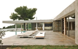 Stone walls, a pine tree exploding out of a deep overhang, iroko decking, outdoor rooms, a glassy swimming pool, and endless views of the sea make this home a paragon of indoor-outdoor living.