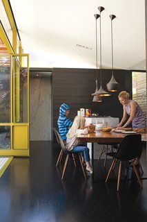 Cal and Macy enjoy a snack from Mom at the almost 14-foot-long walnut slab table sourced from Arborica in Marshall, California. The wood came from a tree that fell into a Palo Alto, California, street. A trio of Tom Dixon Beat Lamps provide the perfect counterpoint to a slew of black plastic Eames shell chairs from Herman Miller.