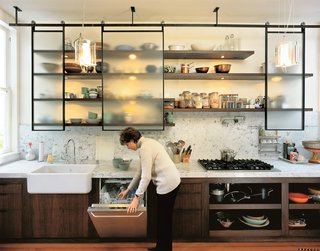 The Felds’ new kitchen is clean, modern, and laced with industrial touches (laboratory faucets, lab glass pendant lamps designed by Sand, stainless steel appliances) while animated by materials and crafted elements that radiate warmth: fir floors unearthed from beneath two layers of linoleum; a fireclay farm sink made in England; Carrera marble counters that extend up the walls; walnut shelving; and industrial mechanisms that put the hardware on display, such as the suspended rolling blackboard that conceals the water heater.