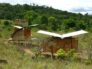 Two housing models perch lightly in a field, both featuring gently curved, rainwater-catching butterfly roofloines.