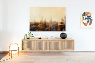 These Shop Owners Have a Killer Apartment Right Upstairs - Photo 7 of 10 - These include the Cesta floor lamp by Miguel Milá and the wall cabinet by Studio Junction in the living room. The photograph hanging above the cabinet is by Joshua Jensen-Nagle. A ceramic dove—a vintage piece by the sculptor Cleo Hartwig—shares space with an antique Zulu beer pot. The painting is by Max Papart.