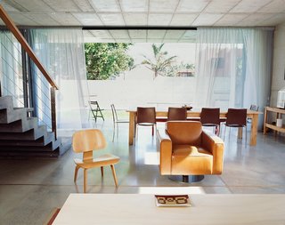 Cognizant of concrete’s excessive greenhouse gas emissions, Gregory built with the future in mind: The modular structure of his home could just as easily accommodate the demands of a nursery, restaurant, or office, as suggested by the various seating and dining arrangements situated throughout the house, particularly in the dining and living area. The space is outfitted with an Eames chair and an unfinished wood shelving unit and dining table. The room opens to the yard and pool, enhancing the room’s circulation to the outdoors.