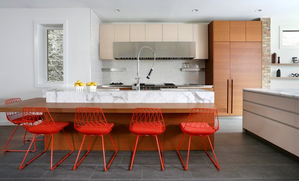 The kitchen features many built-in and hidden features. A Miele integrated refrigerator and freezer are sheathed with custom wood panels and Sub-Zero under-counter refrigerator drawers offer extra space for chilling food. Since the family cooks a lot, Fisher worked with them to incorporate specialty appliances including a Wolf Duel Fuel range, a Wolf deep fryer set into the countertop, a Miele wok burner and dishwasher, and a Panasonic microwave. A custom hood by Best keeps the space ventilated. Calcutta Gold marble adds a striking contrast to the Modulnova cabinetry and island units are from McDuffee Design. The faucet—which boasts an extra-strong spray—is by KWC. Photo 4 of Lakeview modern home