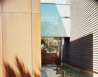 The frosted-glass bridge unites the original 1950s structure (right) to the new addition, which is sheathed in Cor-ten steel panels.
