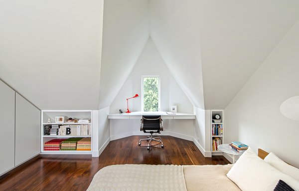 “I love the master bedroom, with the geometry of the white-painted, angled roof lines and the varying shadows that this creates,” Dubbeldam says. The naturally lit space features built-in shelves and a floating desk that overlooks the street below through a tiny window. An aluminum Eames task chair and a Serge Mouille wall light adorn the space. Photo 7 of Contrast House modern home