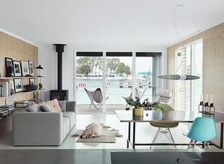 Life for the couple centers on an open kitchen-dining-living area. Nautical references are kept to a minimum, but a few touches nod toward the home’s habitat. A Rais wood-burning stove recalls a ship’s furnace; soft green and blue fiberglass Eames chairs echo the color of the sea, which is a constant presence thanks to floor-to-ceiling glass doors. The custom dining table sits beneath a sculptural Titania pendant by Alberto Meda. Their yellow Labrador, Buster, rests next to a Hay sofa. 